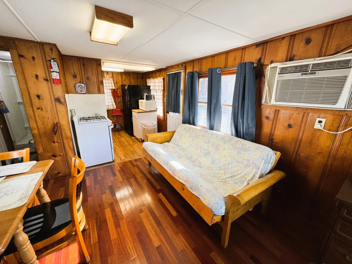 A warm, welcoming interior featuring wood-paneled walls, a plush sofa, a dining table, and visible kitchen appliances. The space is open and inviting, with comfortable furnishings that encourage relaxation and socializing. The overall mood is cozy, perfect for unwinding after a day on the lake.