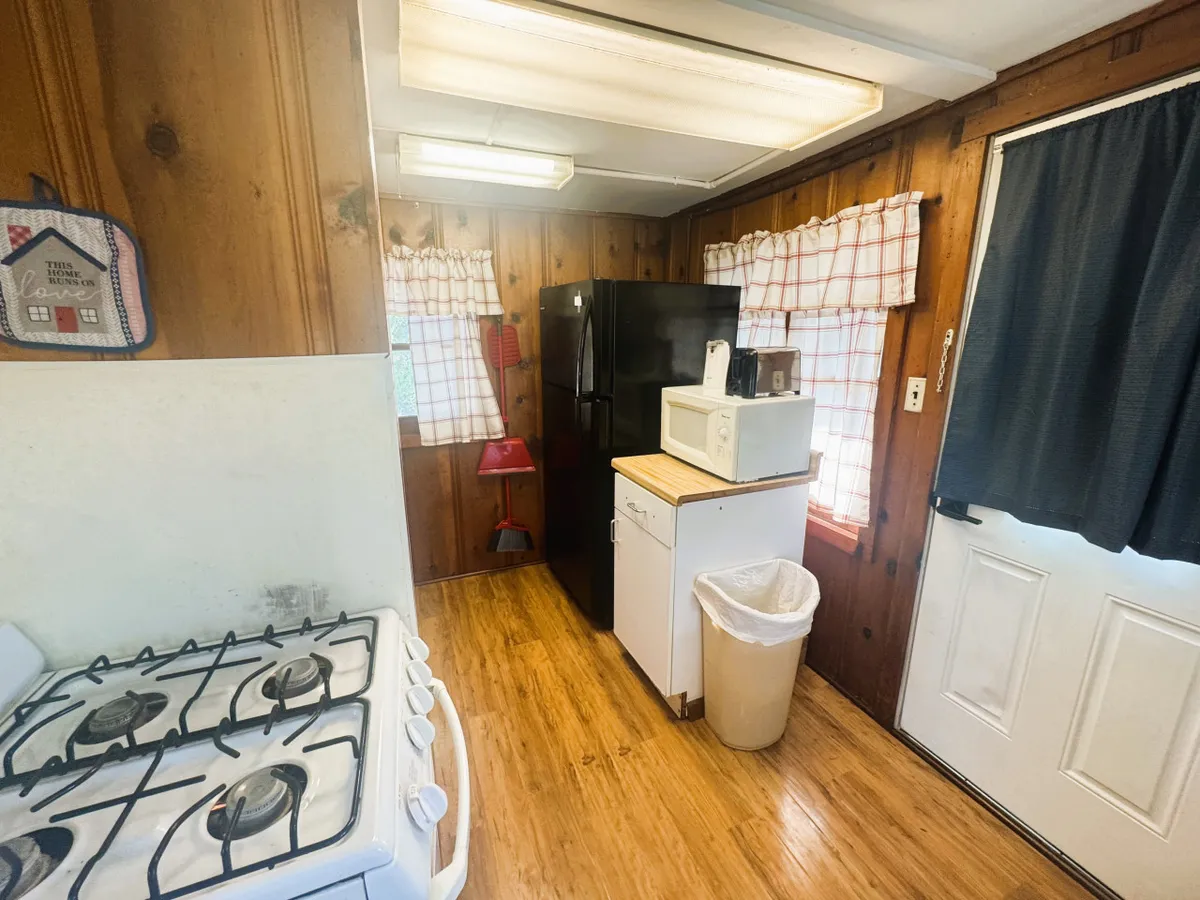 This image showcases a homey kitchenette equipped with a stove, a black full-sized refrigerator, a microwave, and white cabinetry. The scene is bright and inviting, suggesting a practical and comfortable space for preparing family meals.