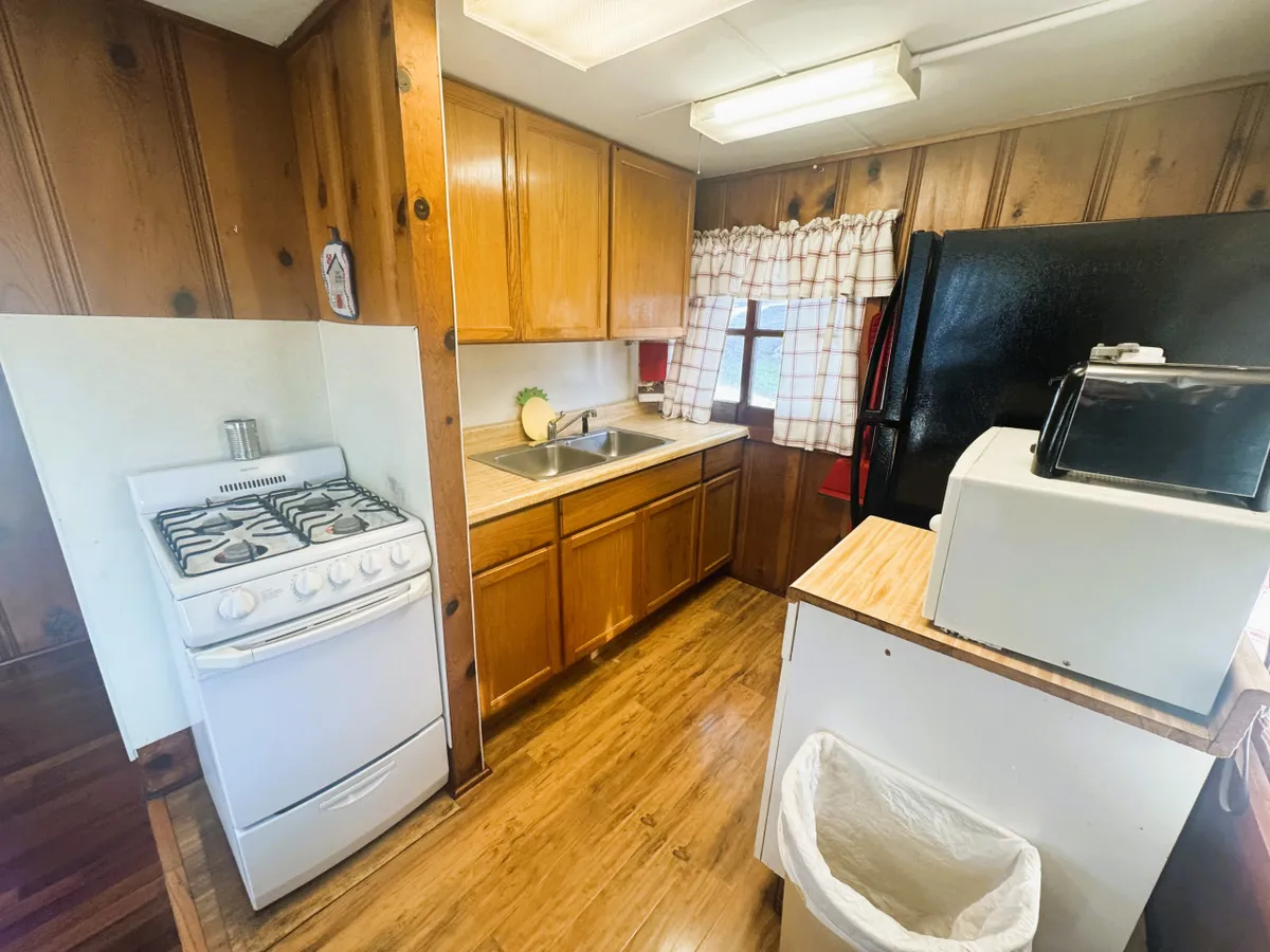 A close-up view of the kitchenette area, featuring a gas stove, sink, wooden cabinets, and a window with charming curtains. The functional layout and warm finishes make it easy to prepare meals or snacks after time outdoors.
