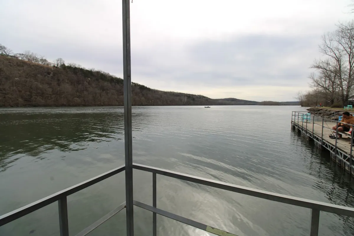A tranquil view of calm water, a distant pier, and rolling hills under a soft sunset glow. The setting is undisturbed, evoking a sense of quiet reflection and natural beauty.